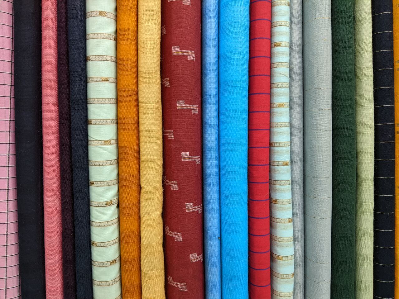 A vibrant selection of fabric rolls in various colors and patterns displayed in a vertical stack.
